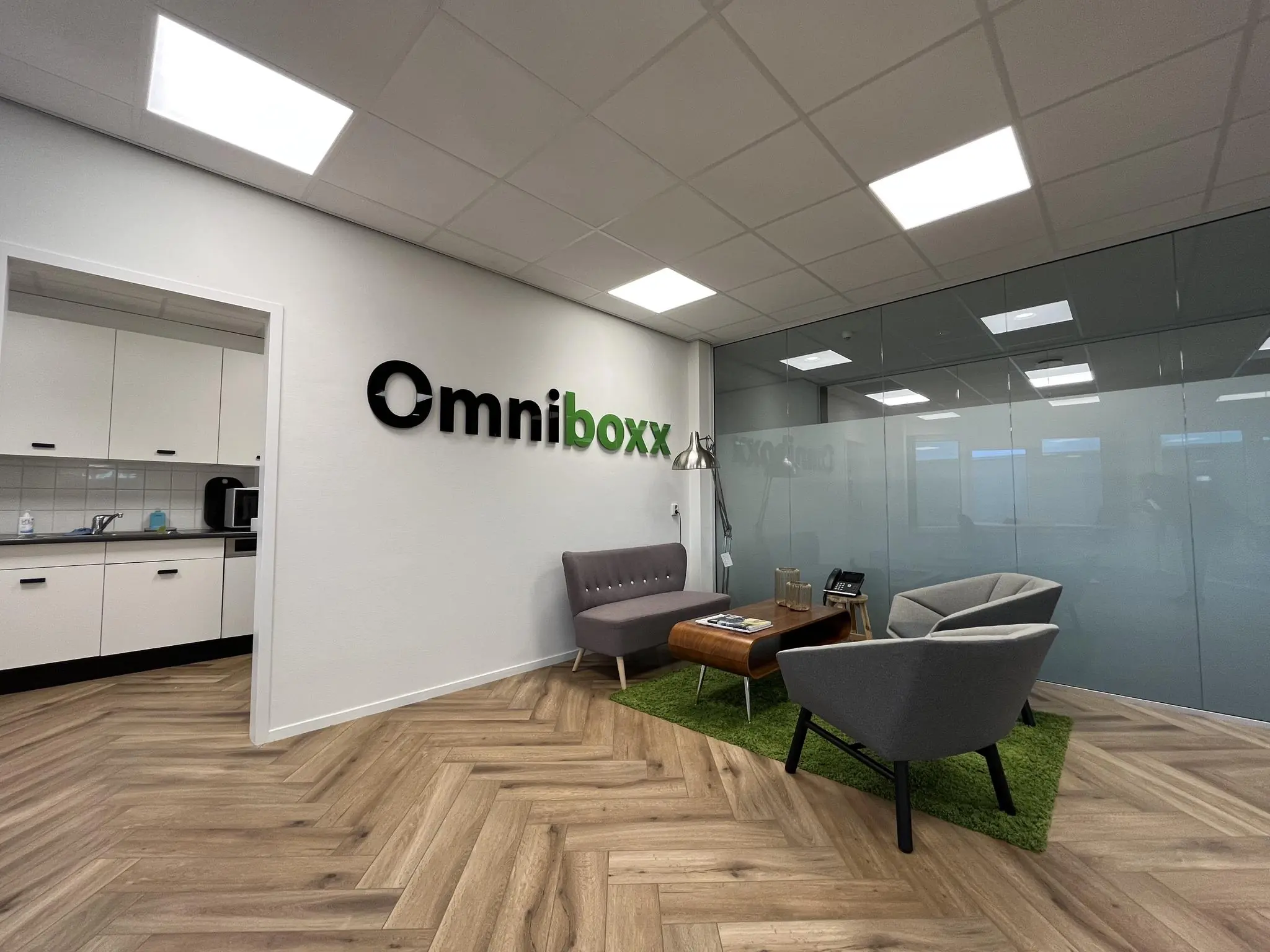 Moderne wachtruimte bij Omniboxx met zithoek, glazen wand en kitchenette.